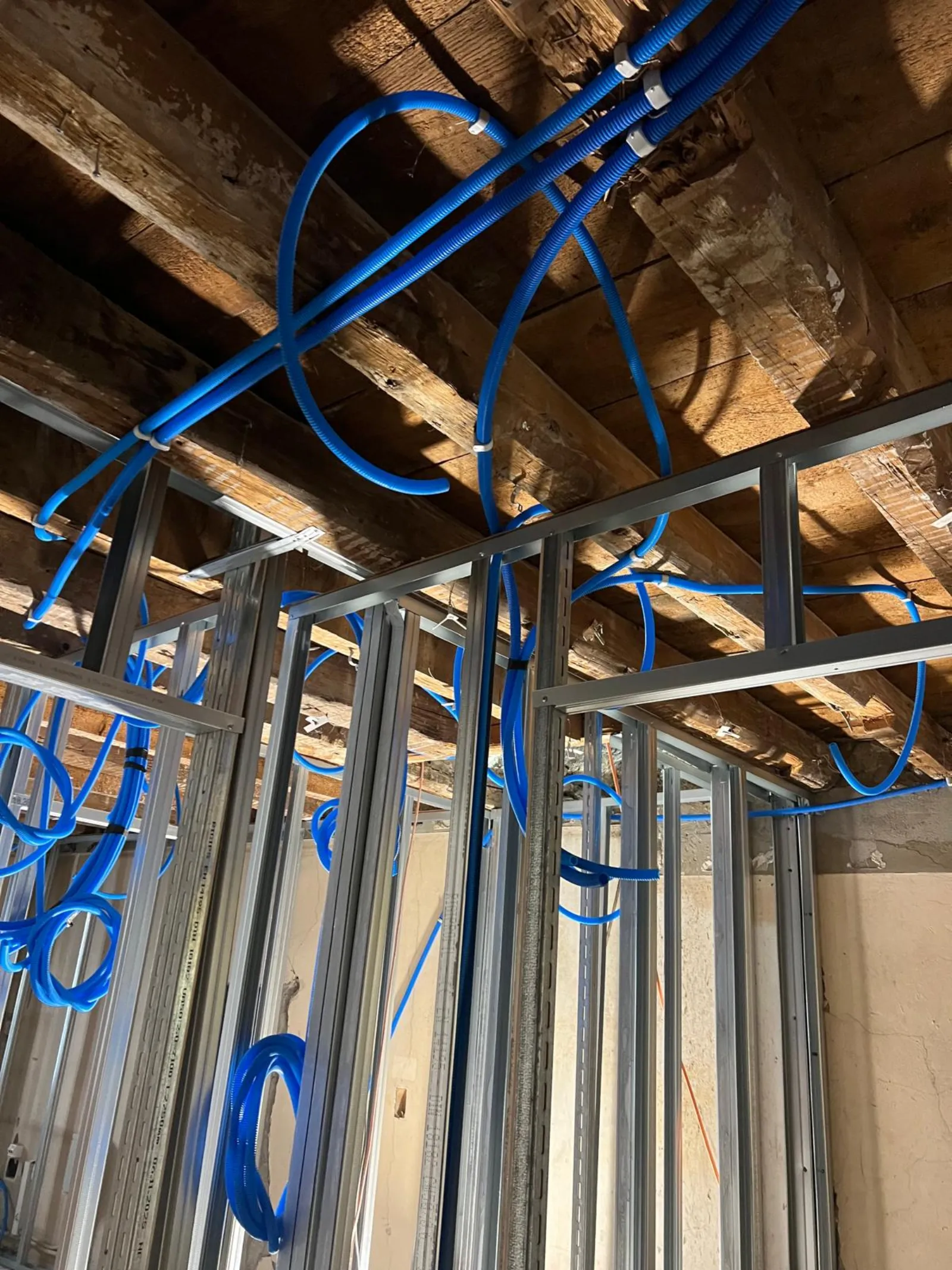 Plafond rampant avec gaines électriques bleues fixées sur poutres