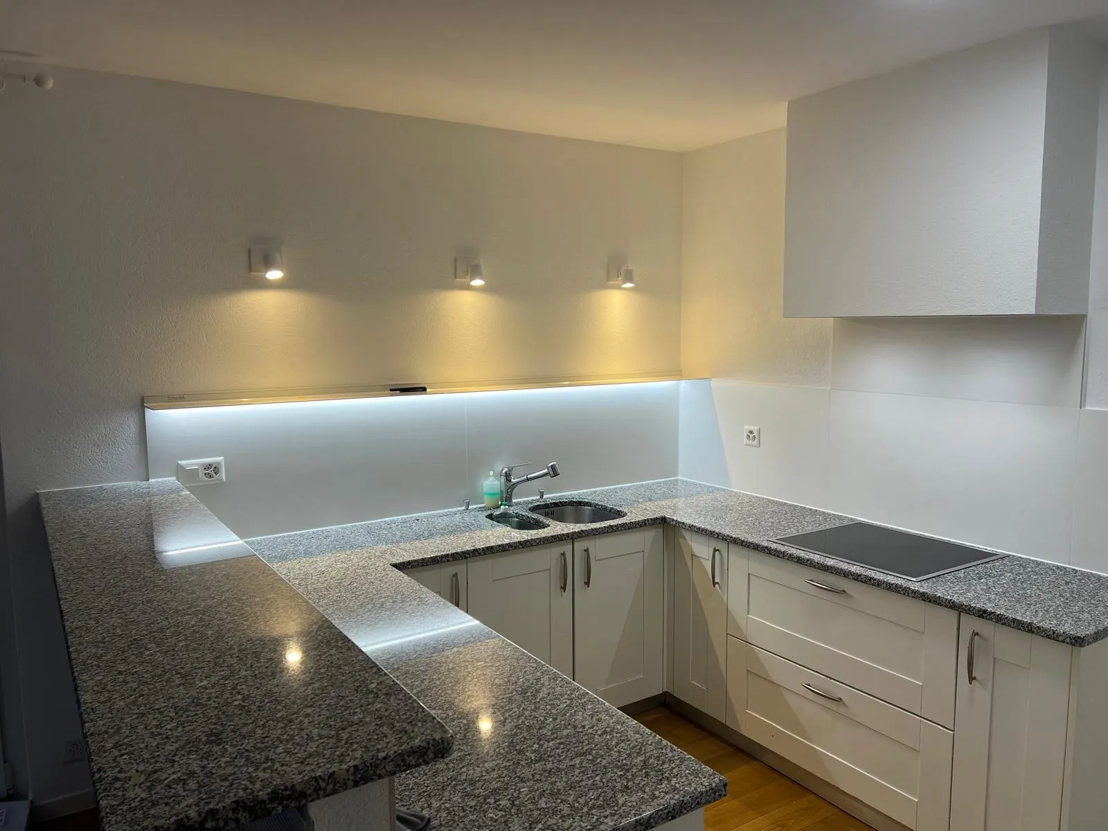 Cuisine en U rénovée avec spots LED, ruban LED bandeau et plan de travail granit gris — après rénovation