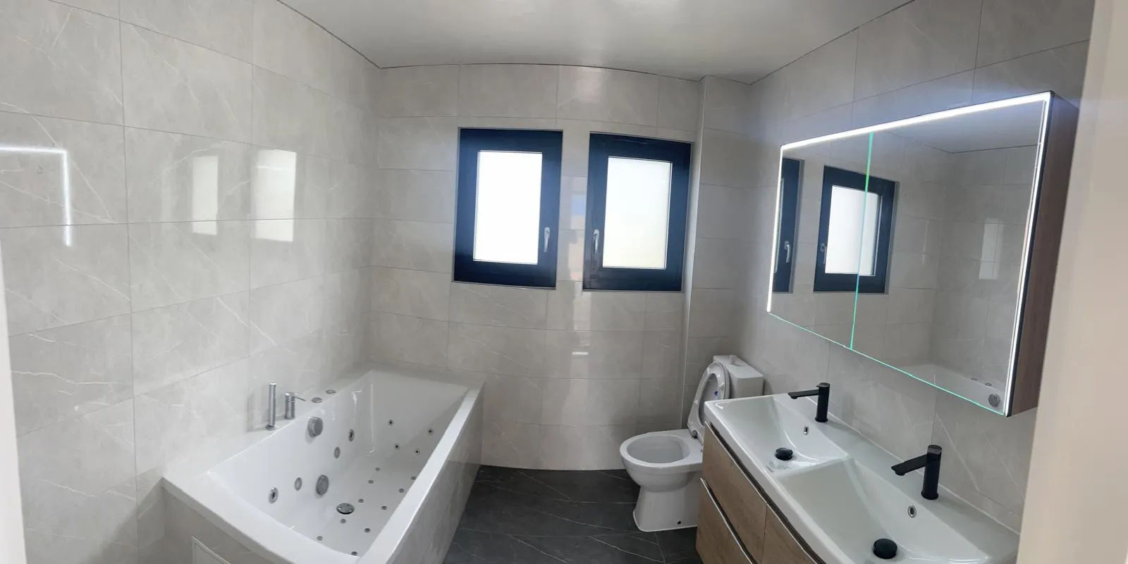 Salle de bain rénovée marbre clair, baignoire balnéo, double vasque et miroir LED — après rénovation